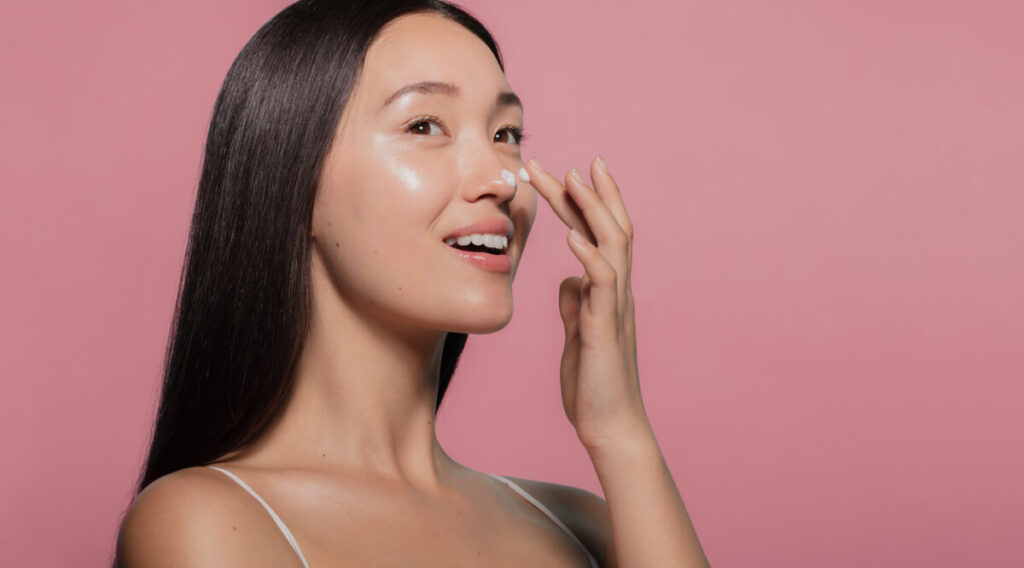 youthful female model applying moisturizer to her face