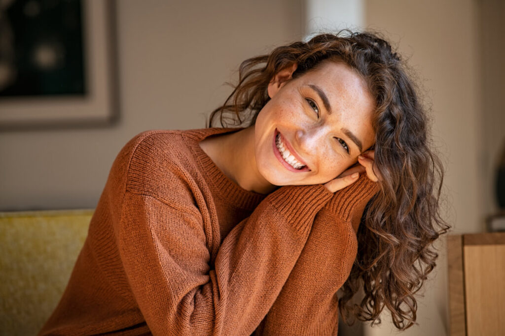 Happy young woman sitting on sofa at home and looking at camera